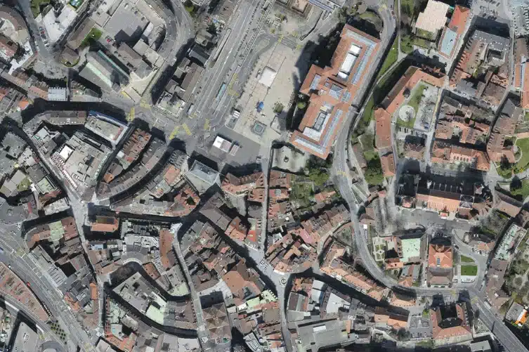 Drone kartoitus ilmakuva kaupungin monimutkaisesta rakenteesta, jossa on kiemurtelevia katuja, tiiviitä rakennuksia sekä modernin ja historiallisen arkkitehtuurin sekoitusta.